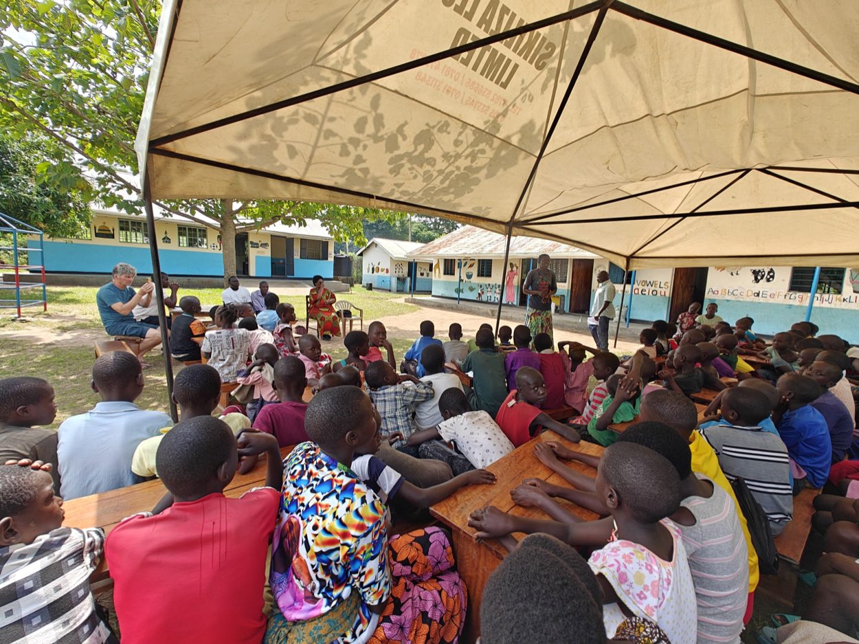 Kinderen en begeleiders samen onder een Sikiliza Leo-tent op het schoolterrein in Mulanda.